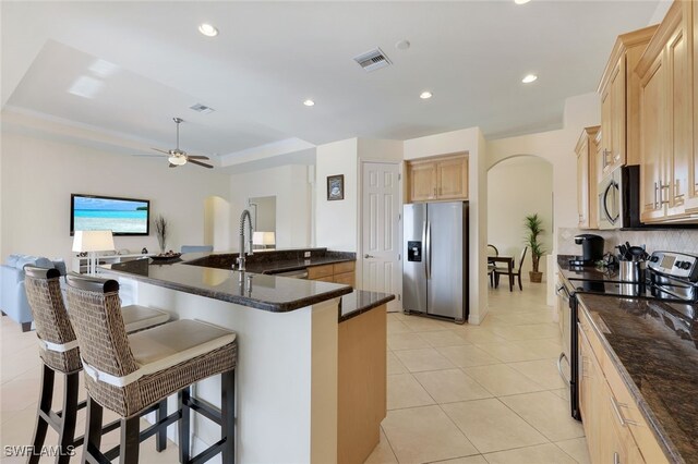 kitchen featuring a tray ceiling, stainless steel appliances, ceiling fan, and light brown cabinets