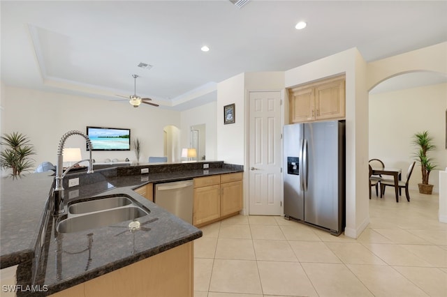 kitchen with stainless steel appliances, a tray ceiling, sink, and dark stone countertops