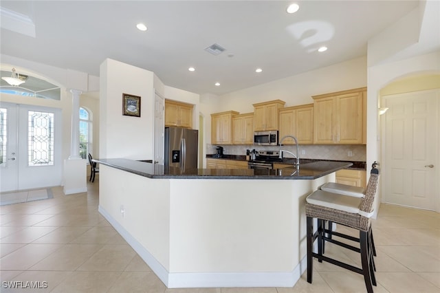 kitchen featuring appliances with stainless steel finishes, light brown cabinets, kitchen peninsula, and decorative backsplash