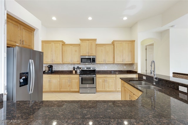 kitchen featuring light brown cabinetry, sink, dark stone counters, stainless steel appliances, and decorative backsplash