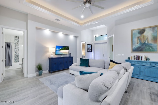 living room with ceiling fan with notable chandelier, light hardwood / wood-style flooring, and a tray ceiling