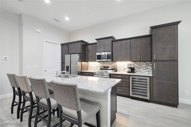 kitchen with beverage cooler, appliances with stainless steel finishes, tasteful backsplash, sink, and a center island with sink