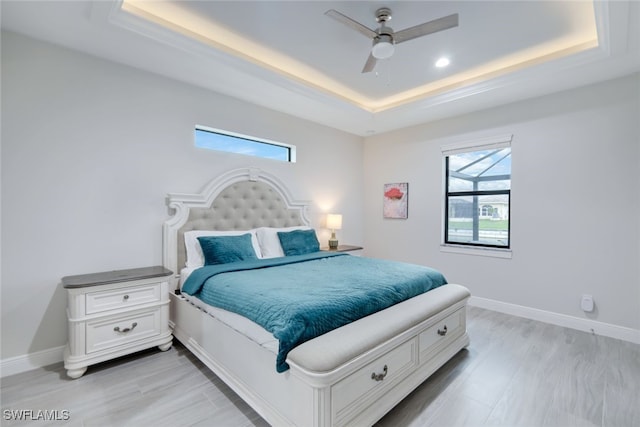 bedroom with ceiling fan, light hardwood / wood-style flooring, and a tray ceiling