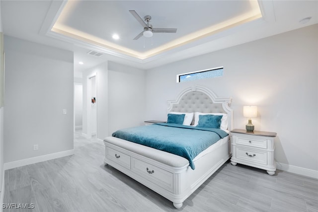 bedroom with ceiling fan, a tray ceiling, and light hardwood / wood-style flooring