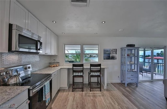 kitchen featuring light hardwood / wood-style floors, light stone countertops, white cabinetry, and appliances with stainless steel finishes