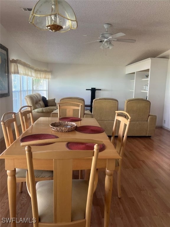 dining room featuring visible vents, a textured ceiling, wood finished floors, and a ceiling fan