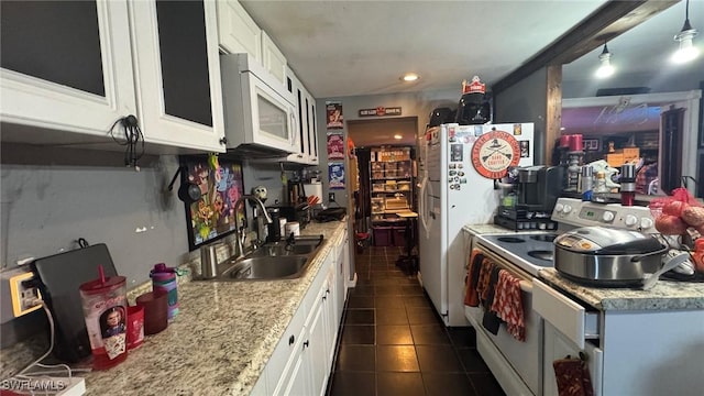 kitchen with white appliances, dark tile patterned flooring, light stone counters, white cabinets, and sink