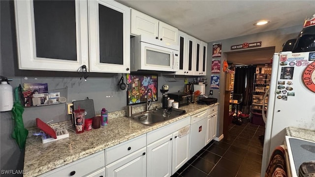 kitchen featuring white appliances, dark tile patterned floors, light stone counters, white cabinets, and sink