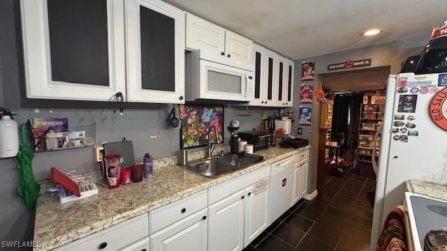 kitchen with white appliances, white cabinets, a sink, and dark tile patterned flooring