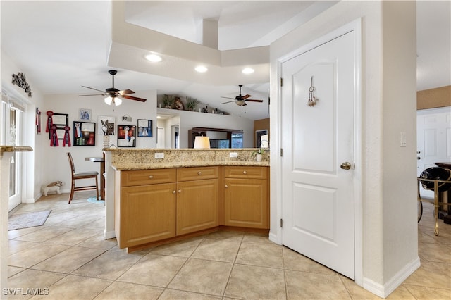 kitchen featuring kitchen peninsula, ceiling fan, light tile patterned flooring, lofted ceiling, and light stone counters