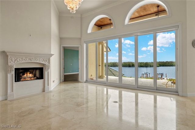 unfurnished living room with an inviting chandelier, a warm lit fireplace, ornamental molding, a water view, and marble finish floor