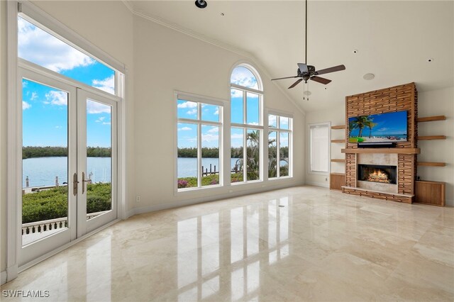 unfurnished living room featuring a towering ceiling, french doors, a fireplace, a water view, and ceiling fan