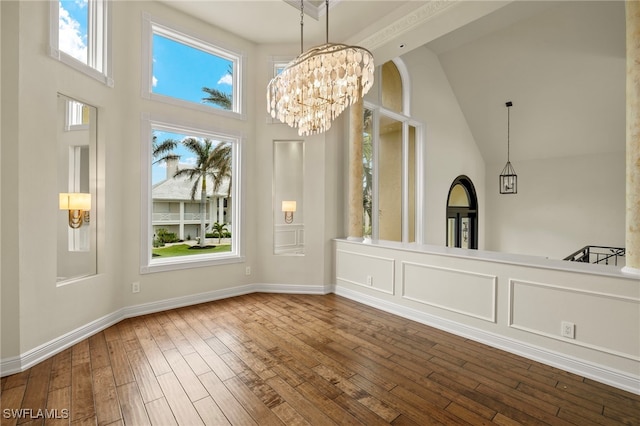 unfurnished dining area featuring baseboards, an inviting chandelier, wood finished floors, and a towering ceiling