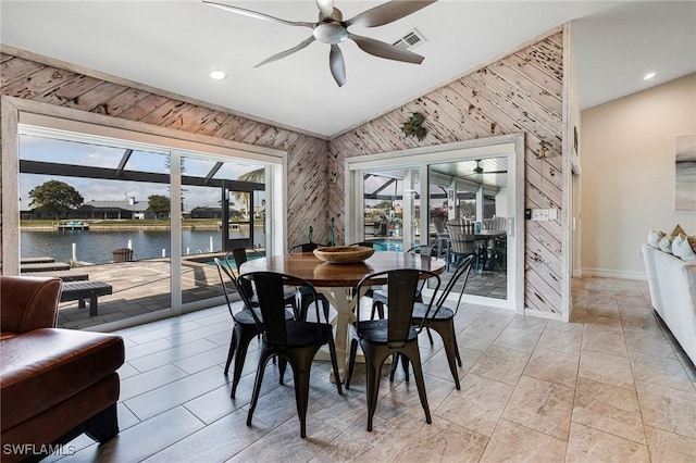 dining space featuring a water view, ceiling fan, and wood walls