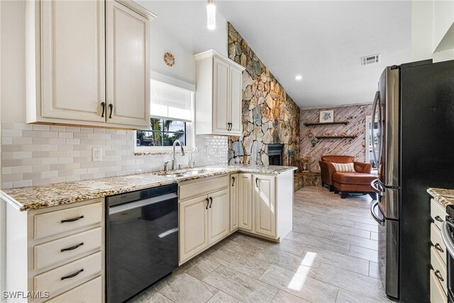 kitchen with dishwasher, cream cabinets, light stone counters, and stainless steel refrigerator