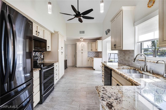 kitchen with tasteful backsplash, sink, light stone counters, black appliances, and cream cabinets