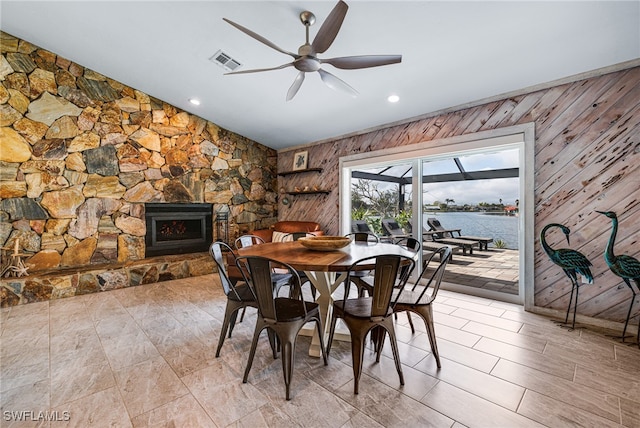 dining room with ceiling fan, a water view, a fireplace, vaulted ceiling, and wood walls