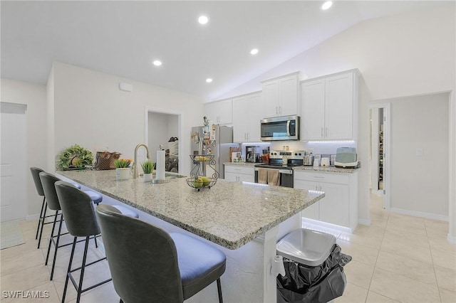 kitchen with stainless steel appliances, light stone countertops, white cabinets, a kitchen bar, and vaulted ceiling