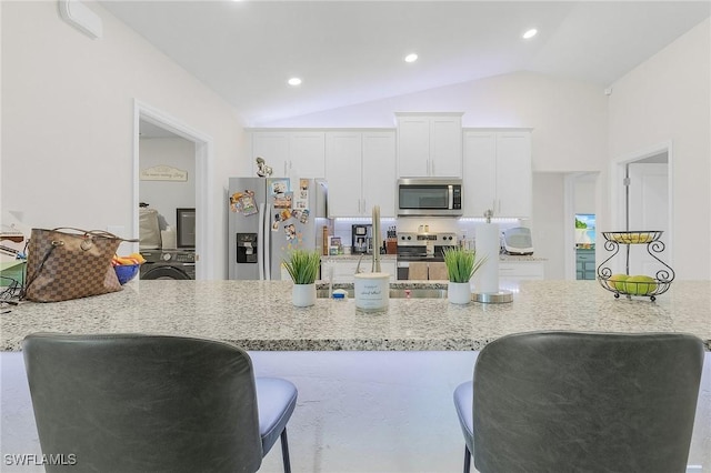 kitchen featuring stacked washing maching and dryer, appliances with stainless steel finishes, vaulted ceiling, white cabinetry, and light stone countertops