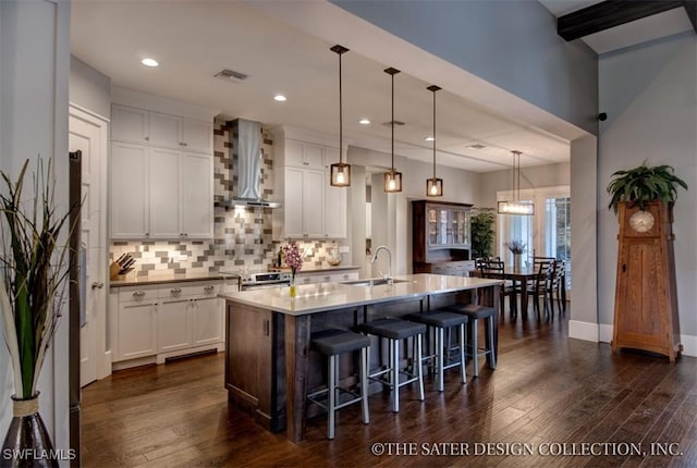 kitchen featuring hanging light fixtures, wall chimney exhaust hood, sink, white cabinetry, and a kitchen island with sink