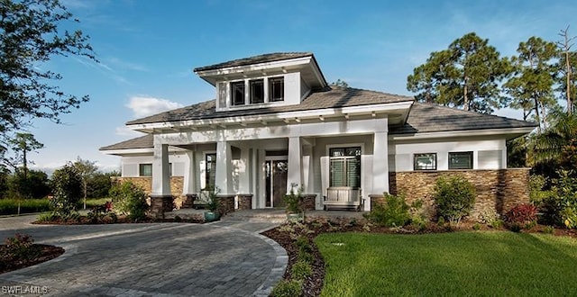 view of front of property featuring covered porch, stone siding, a front lawn, and stucco siding