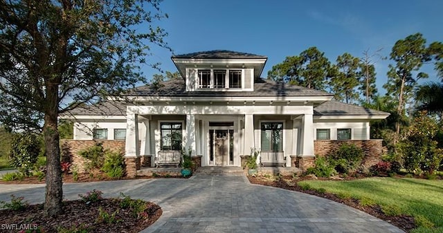 view of front of property with stone siding, a porch, decorative driveway, and a front lawn