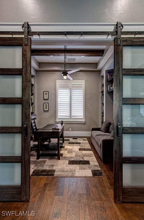 interior space with a barn door, beamed ceiling, dark wood finished floors, and baseboards