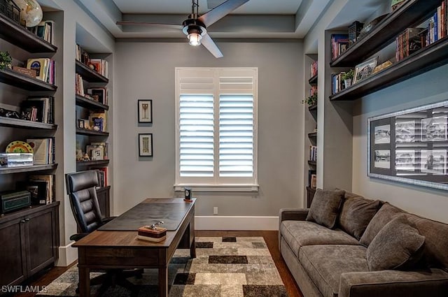 home office featuring built in shelves, ceiling fan, baseboards, and wood finished floors