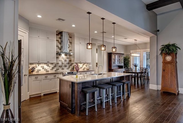 kitchen featuring an island with sink, wall chimney exhaust hood, white cabinetry, and a sink