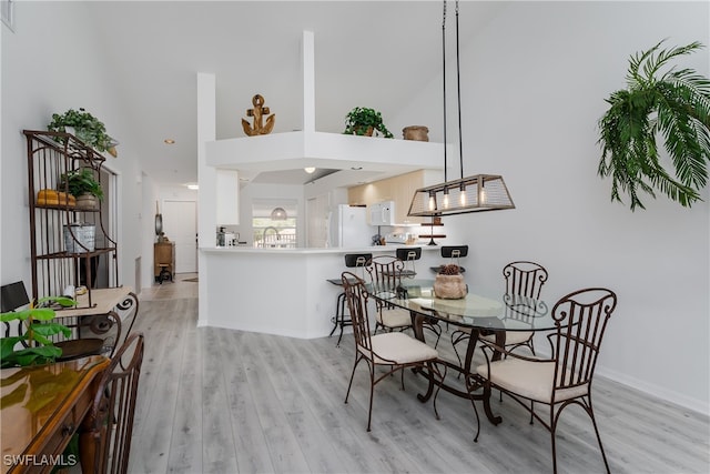 dining area featuring light hardwood / wood-style floors, a towering ceiling, and sink