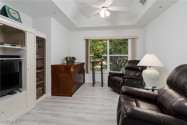 living room with a raised ceiling, ceiling fan, and light hardwood / wood-style flooring