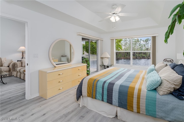 bedroom featuring ceiling fan, access to exterior, light hardwood / wood-style flooring, and a tray ceiling