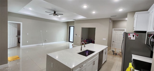 kitchen with sink, white cabinets, a raised ceiling, stainless steel refrigerator, and a kitchen island with sink