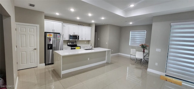 kitchen with stainless steel appliances, sink, white cabinetry, light tile patterned floors, and a kitchen island with sink