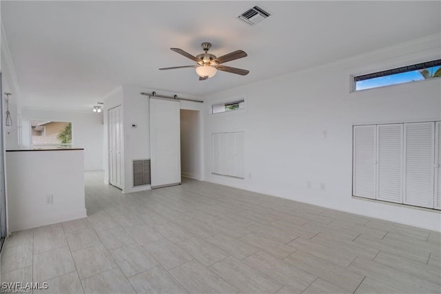 empty room with ceiling fan, a healthy amount of sunlight, and a barn door