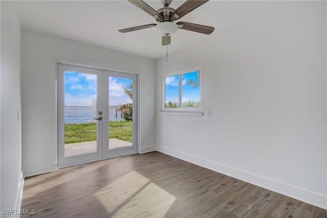 spare room featuring wood-type flooring, a water view, ceiling fan, and french doors