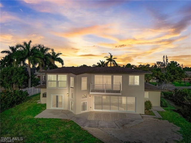 back house at dusk with a balcony, a yard, and a patio area