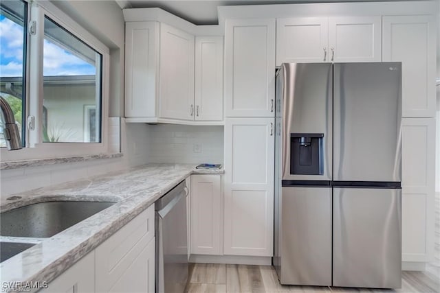 kitchen with sink, appliances with stainless steel finishes, white cabinetry, tasteful backsplash, and light stone countertops