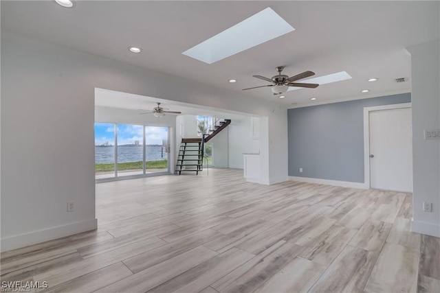 unfurnished living room featuring light hardwood / wood-style flooring, ceiling fan, and a skylight