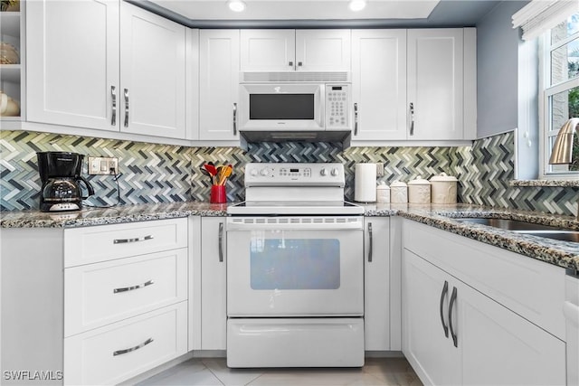 kitchen featuring tasteful backsplash, dark stone counters, white appliances, and white cabinetry