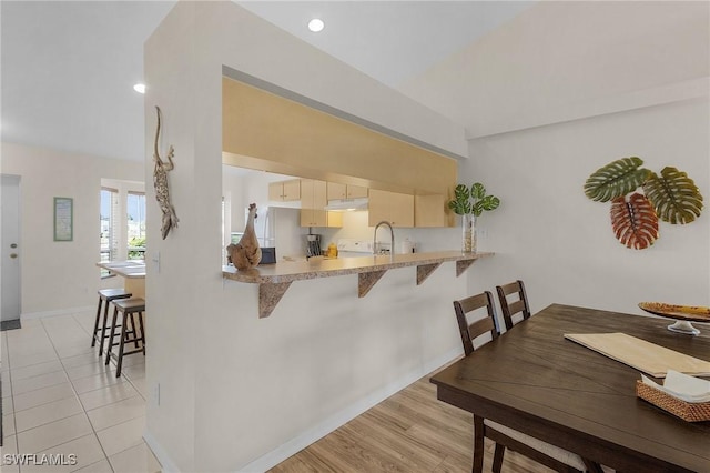 kitchen with a kitchen bar, white fridge, light hardwood / wood-style floors, sink, and kitchen peninsula