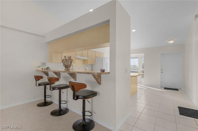 kitchen with light tile patterned floors, white refrigerator with ice dispenser, a kitchen bar, and kitchen peninsula