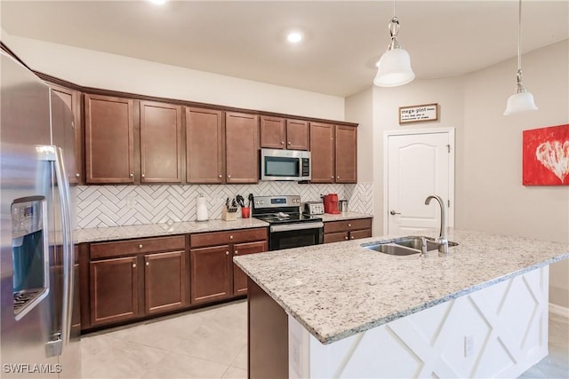 kitchen with light stone countertops, decorative light fixtures, a kitchen island with sink, appliances with stainless steel finishes, and sink