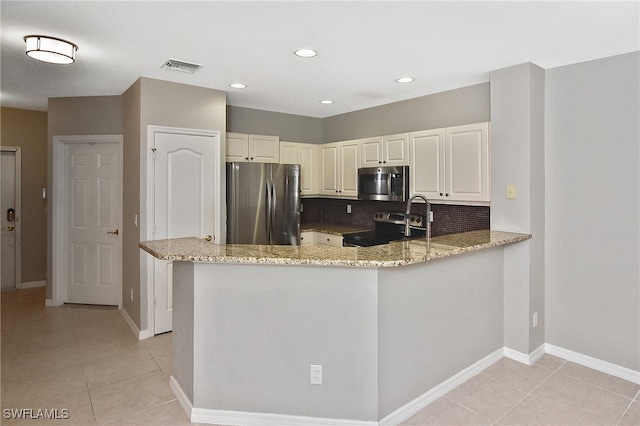 kitchen with tasteful backsplash, kitchen peninsula, appliances with stainless steel finishes, and light stone countertops