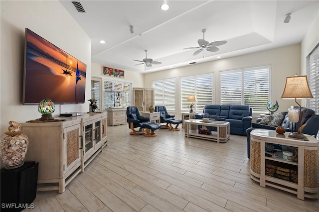 living room with ceiling fan, light wood-type flooring, and a tray ceiling