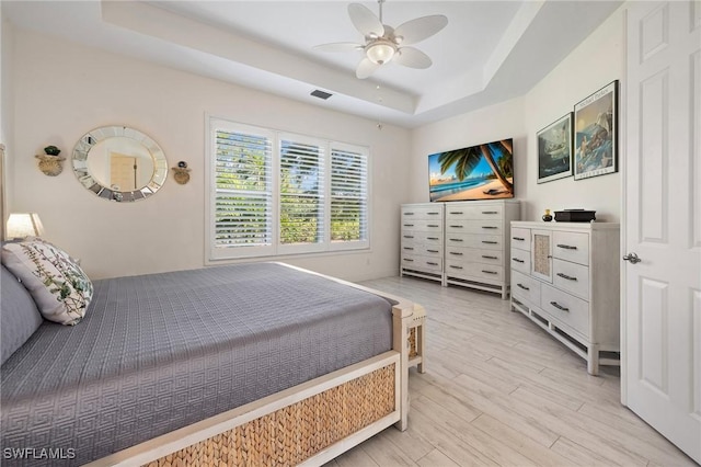 bedroom with ceiling fan, light hardwood / wood-style flooring, and a raised ceiling