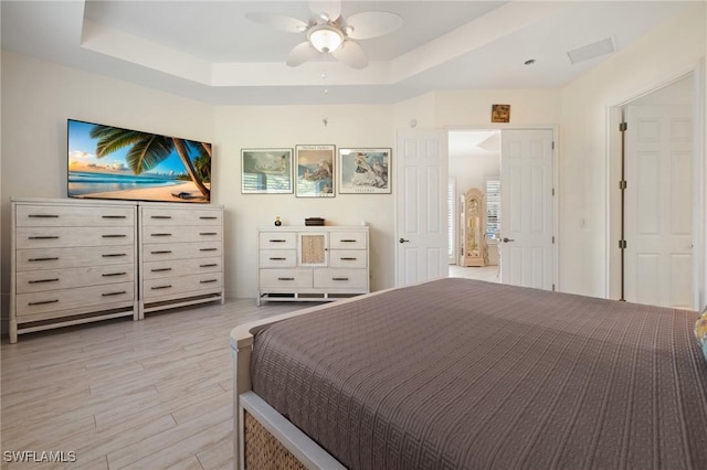 bedroom featuring light hardwood / wood-style floors, ceiling fan, and a tray ceiling