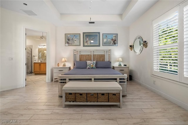 bedroom featuring a tray ceiling, light hardwood / wood-style floors, and connected bathroom