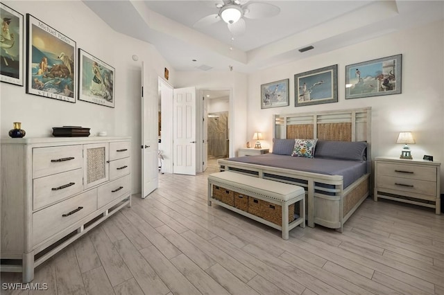 bedroom with light hardwood / wood-style floors, a raised ceiling, connected bathroom, and ceiling fan