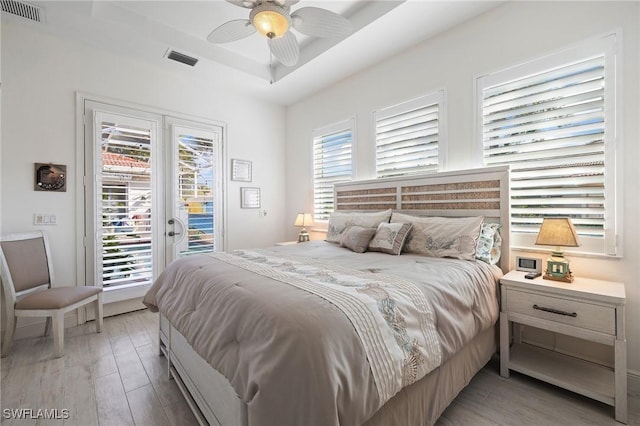 bedroom with light hardwood / wood-style floors, ceiling fan, access to outside, and a tray ceiling